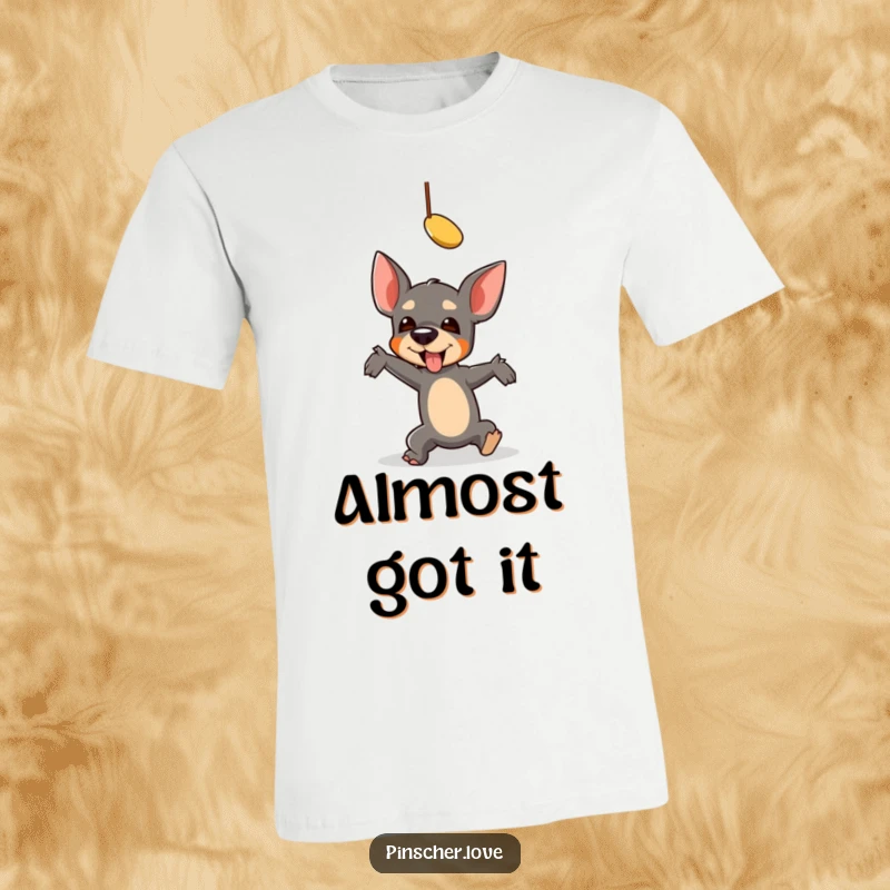 Funny Pinscher T-Shirt: A pinscher comically falls while hilariously reaching for a dangling toy, perfect for a laugh.