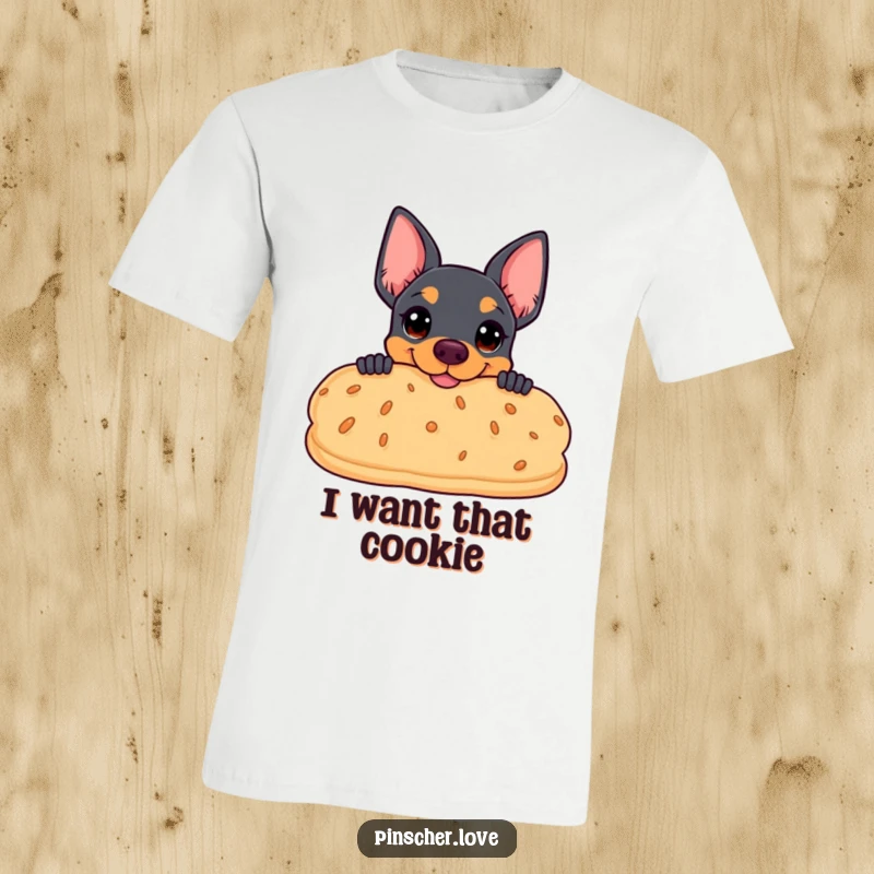 Funny t-shirt featuring a pinscher peeking coyly from behind an oversized, smiling biscuit, capturing a moment of treat anticipation.